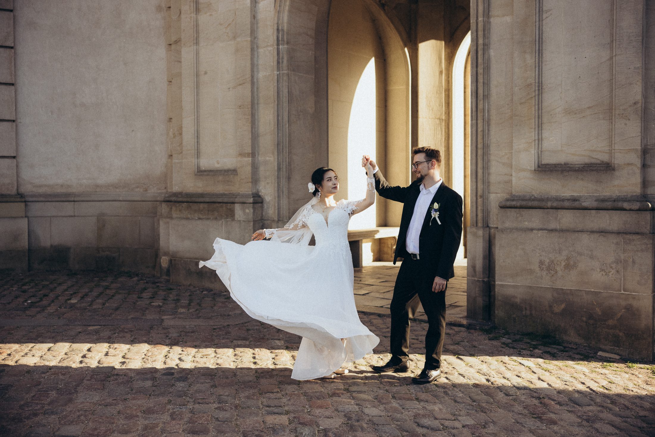 Groom twirling the bride, her dress in motion in the golden light by the arches