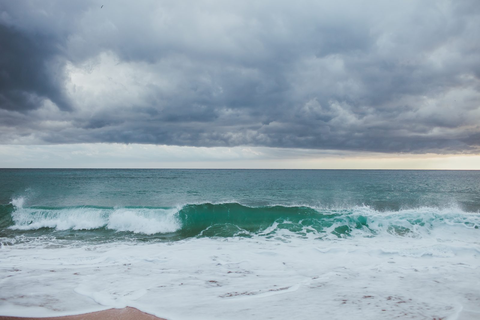 A green wave breaking under storm clouds, Palamos, Spain