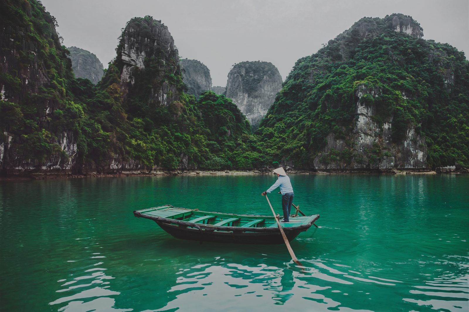 Boatman on turquoise water among karst cliffs, Ha Long Bay, Vietnam